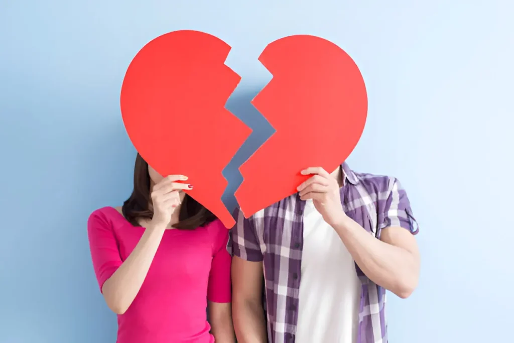 Young couple holding broken heart pieces, showing emotional distance and how to break up with someone with care
